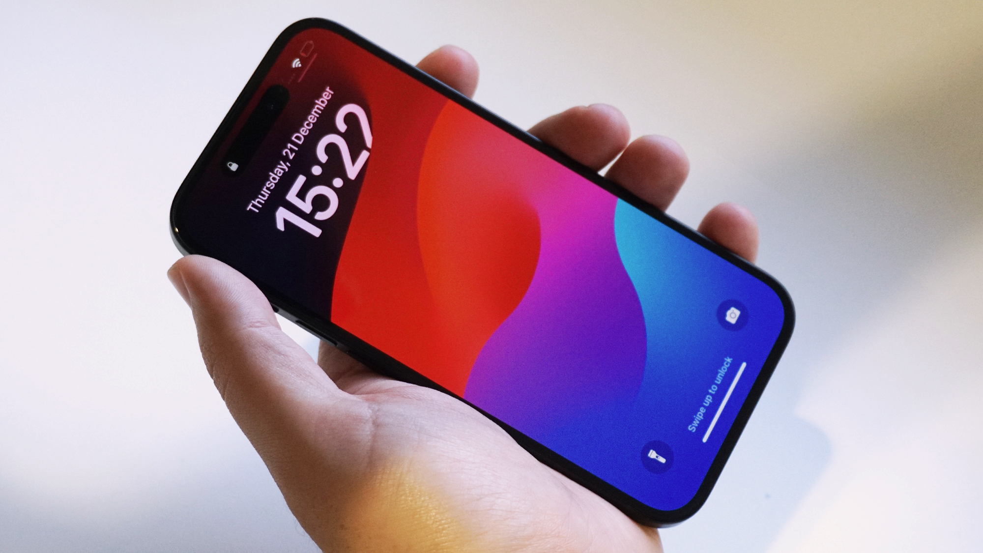 iPhone 15 h&aring;lls upp framf&ouml;r en vit v&auml;gg.