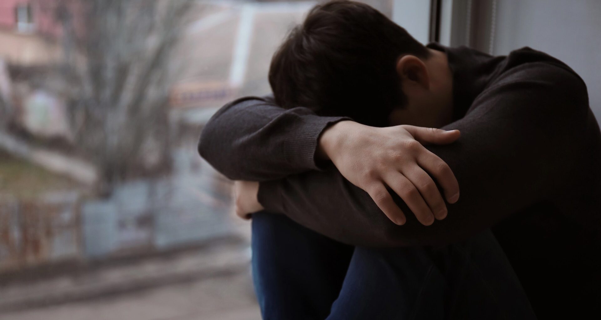 Man sitter intill fönster och gömmer sitt ansikte.