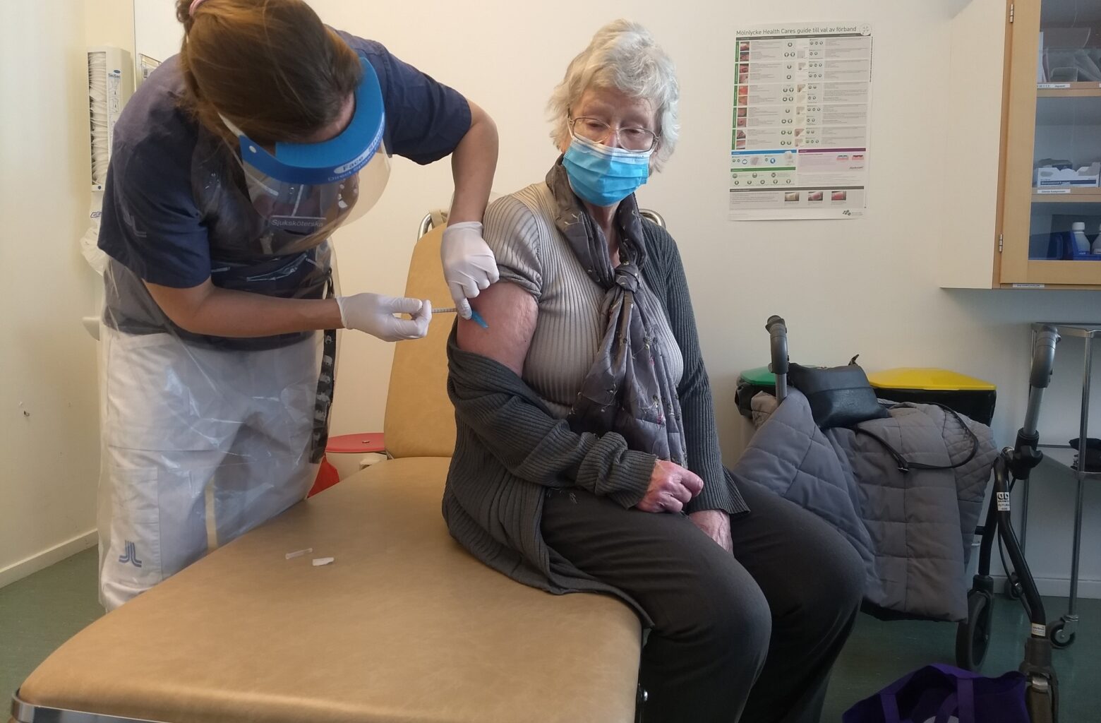 En äldre dam i munskydd får en spruta.