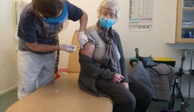 En äldre dam i munskydd får en spruta.