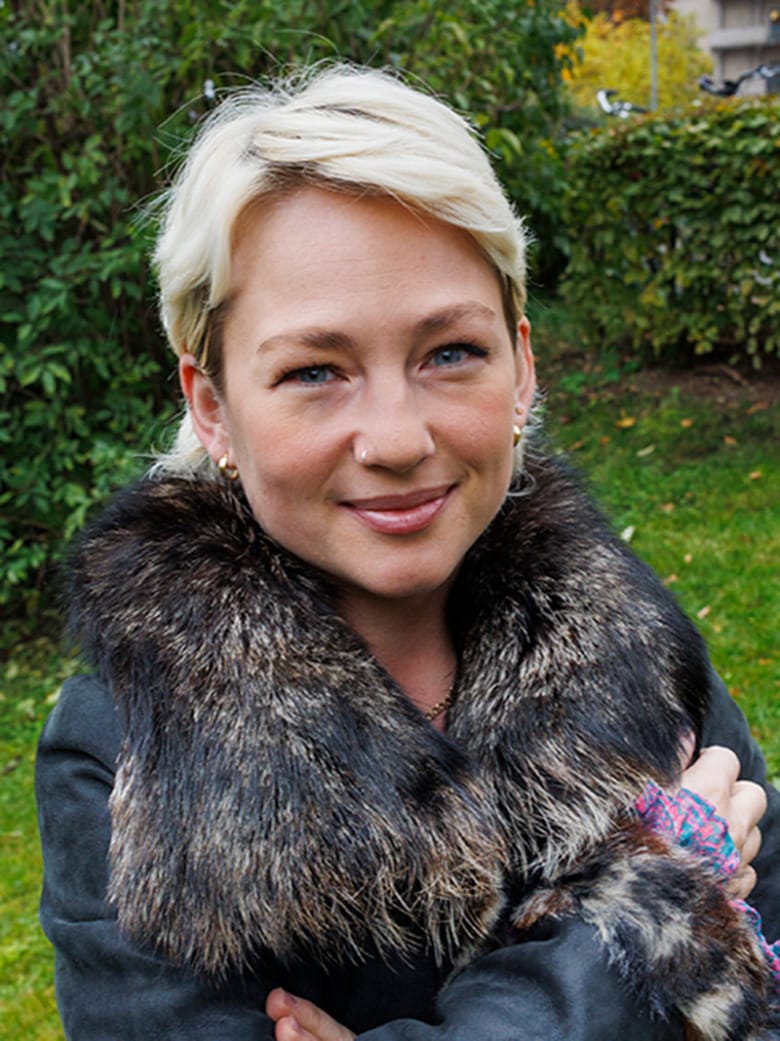 Sjuksköterskan Alexandra Arrhén står utomhus med armarna i kors, i bakgrunden är det en grön gräsmatta och gröna buskar. Hon tittar direkt in i kameran.