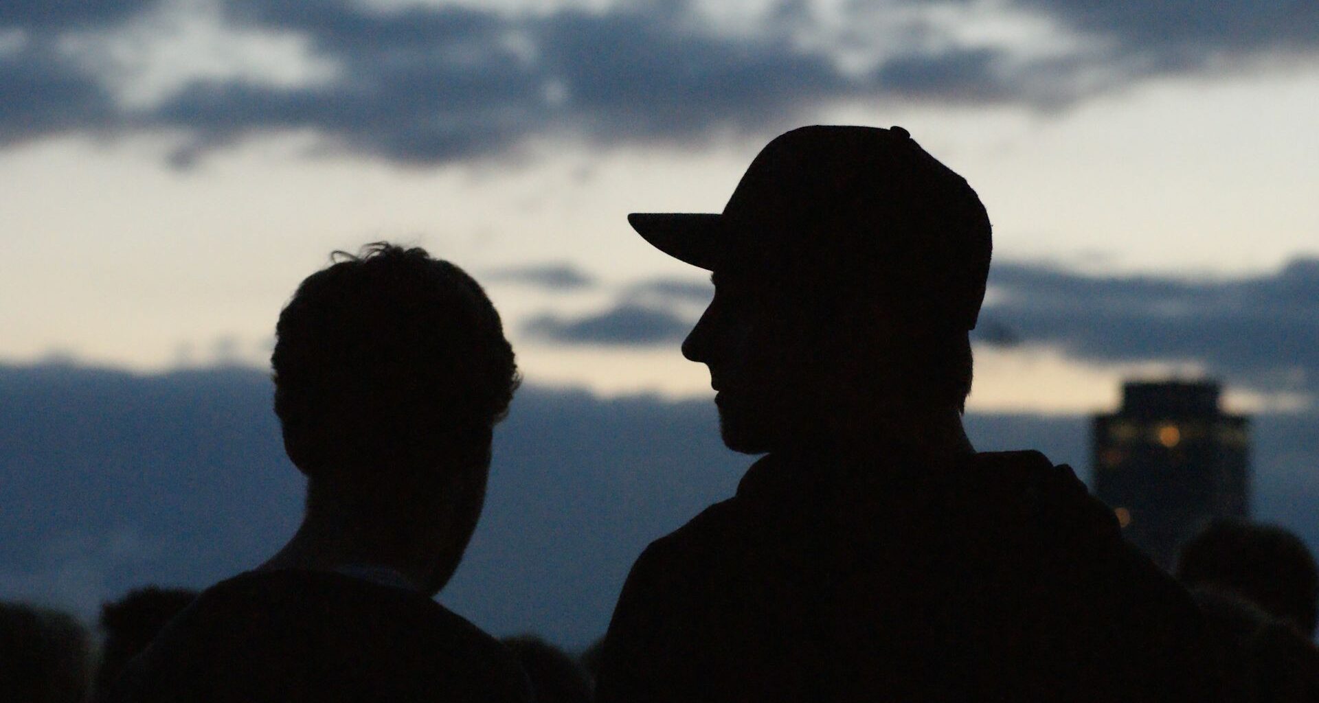 Två unga män, den ena i keps, i svart siluett mot kvällshimmel.