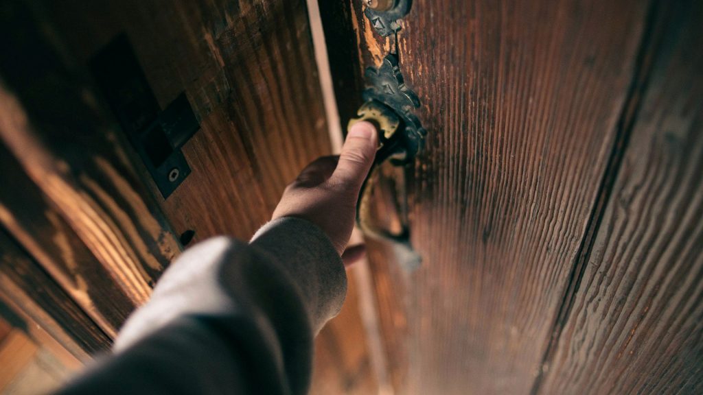 Han som griper om dörrhandtag på gammal trädörr.