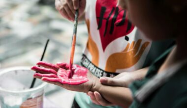 Ett barn målar med rosa färg på ett annat barns handflata, med en pensel.