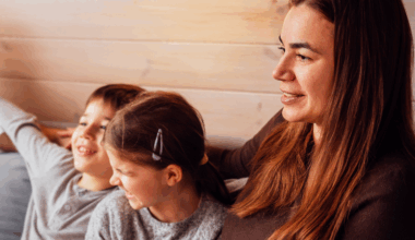 En kvinna med två barn sitter i soffa.