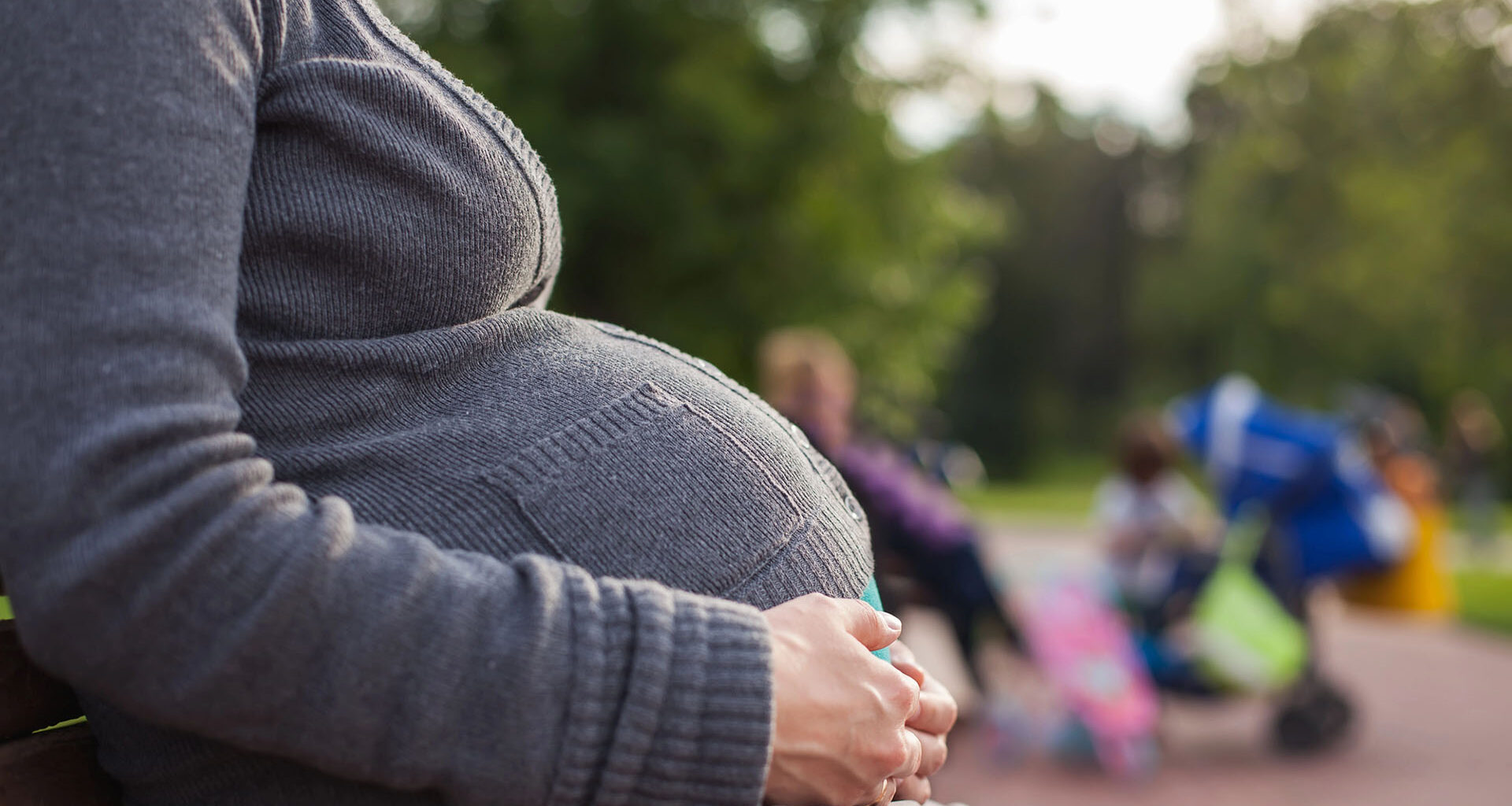 Kvinna med stor mage sitter på en bänk utomhus.