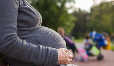 Kvinna med stor mage sitter på en bänk utomhus.