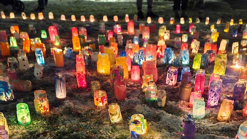 Färgglada ljuslyktor står på mark täckt av snö.