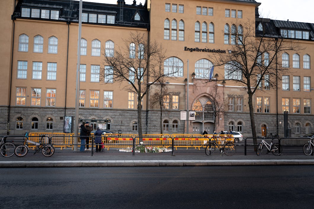 En byggnad med skylten "Engelbrektsskolan", välvda fönster, träd, cyklar och gula avspärrningar vid trottoaren.