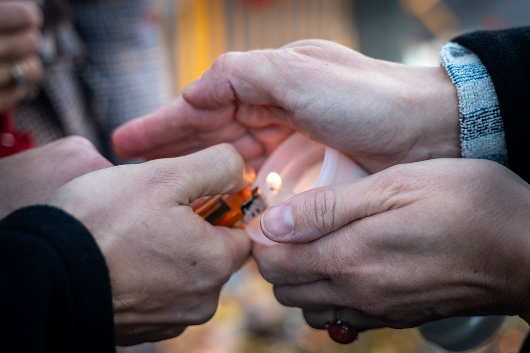 Två händer skyddar ett ljus medan en annan person tänder veken med en tändare utomhus.