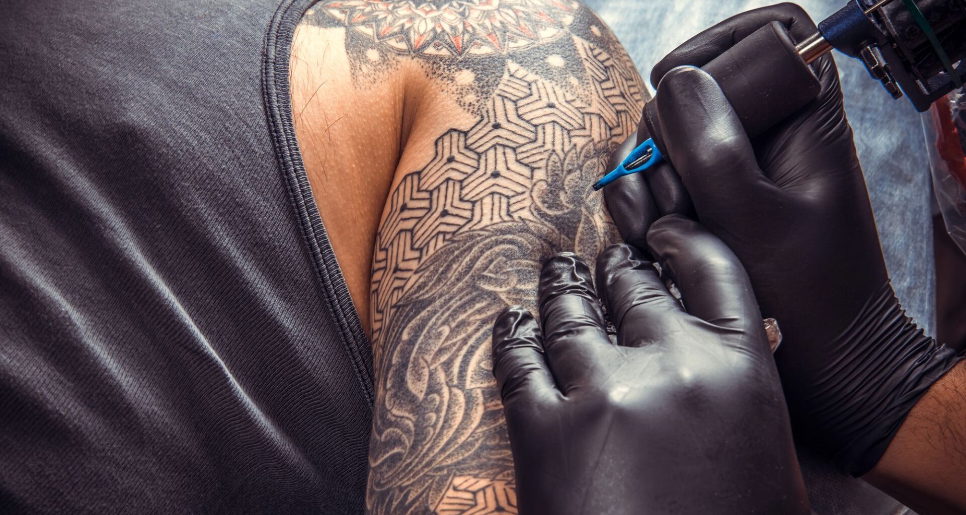 Man får armen tatuerad. Två händer med svarta handskar tatuerar med nål.