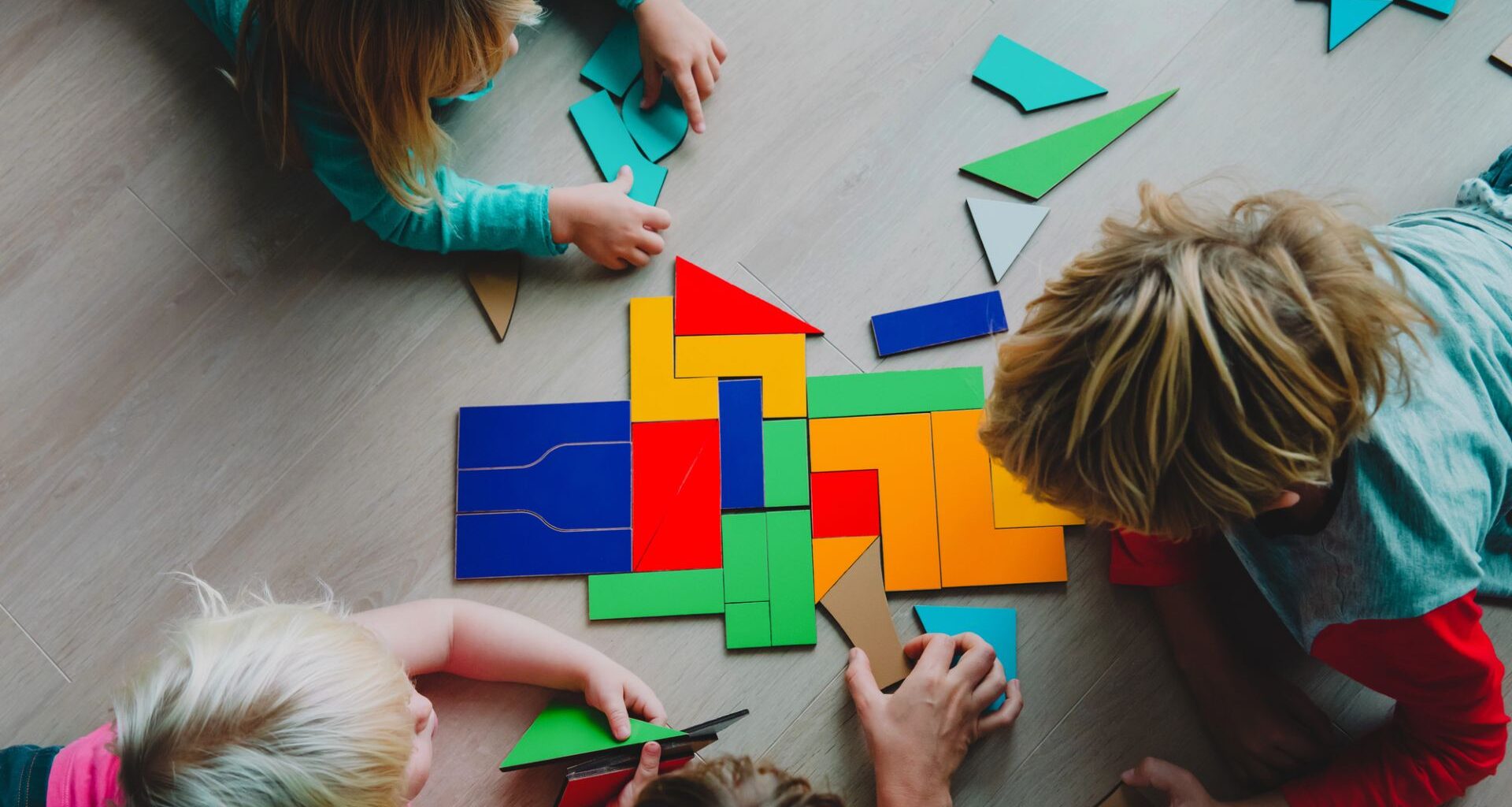 Tre barn i lågstadieåldern leker med pussel på ett ljust trägolv.