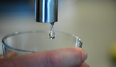 Någon håller ett glas under en droppande vattenkran.