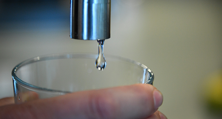 Någon håller ett glas under en droppande vattenkran.