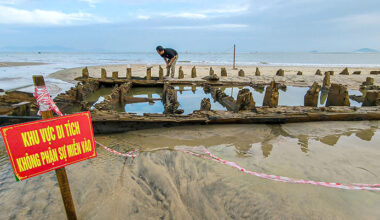 En person står vid vraket som är i sanden och vattnet.