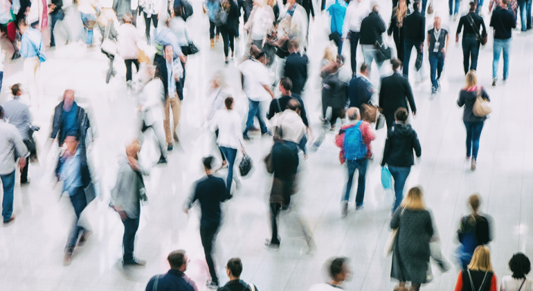 Suddig bild av många människor som går över ett torg eller liknande plats.