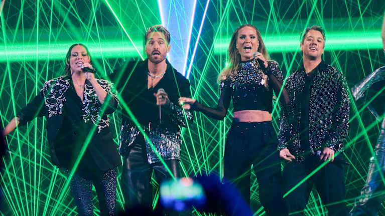 Gruppen framför ett nummer på scenen med spektakulära gröna laserstrålar och färgglad scenbelysning under en musikshow.