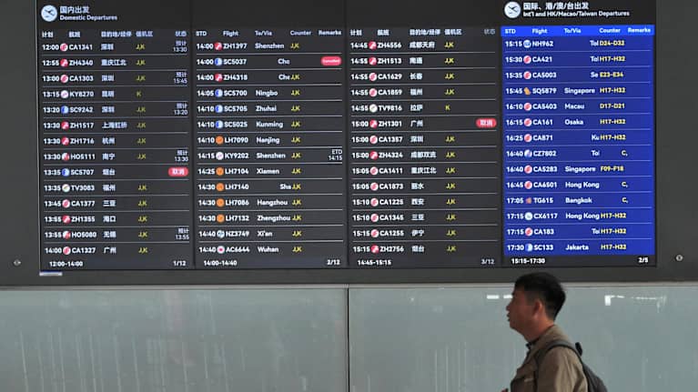 Kinesisk man vandrar förbi en elektronisk informationsskylt med flygtider.