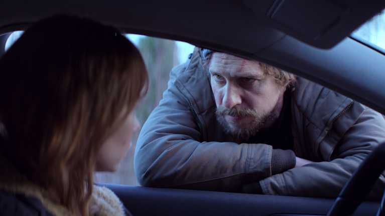 En man i vinterkläder lutar sig in genom ett öppet bilfönster.