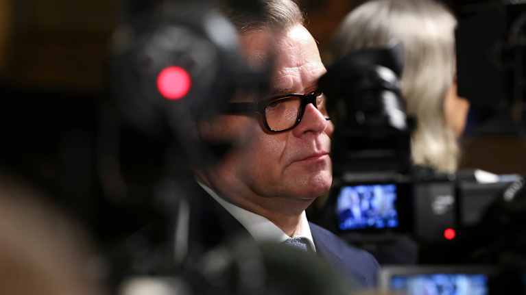 En man står framför flera kameror som syns i förgrunden. Mannen bär kostym och har glasögon.