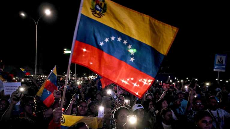 Människor samlade i mörker viftar med Venezuelas flagga och med lysande mobiltelefoner. 