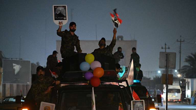 Personer i militärkläder står på en lastbil prydd med ballonger och håller upp skyltar.