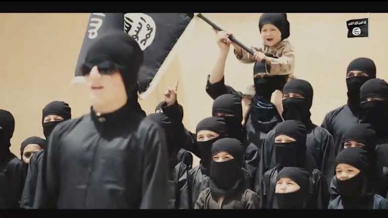 Unga människor i svarta kläder och dukar som täcker ansiktet, en viftar med en IS-flagga.