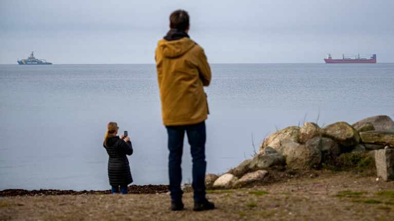 En man och en kvinna står på en strand och tittar ut mot två fartyg. 