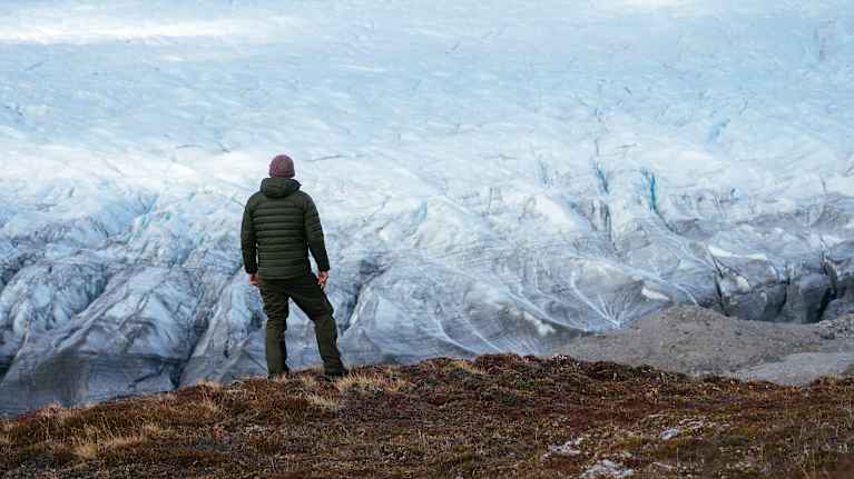 En man står med ryggen mot kameran och tittar ut över en smältande glaciär på Grönland.