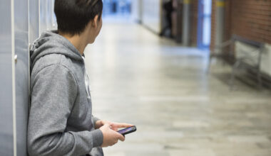 Ung man i täckjacka tittar på sin mobiltelefon.