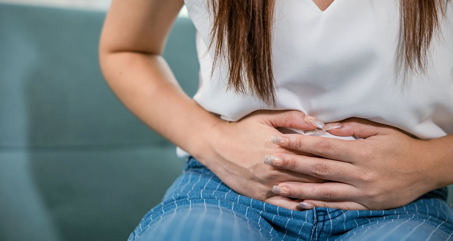 Ung kvinna i vit tröja håller händerna över magen.