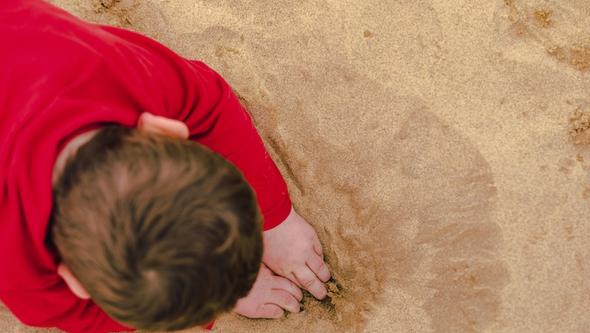 Young boy digging hole in the sand with hands