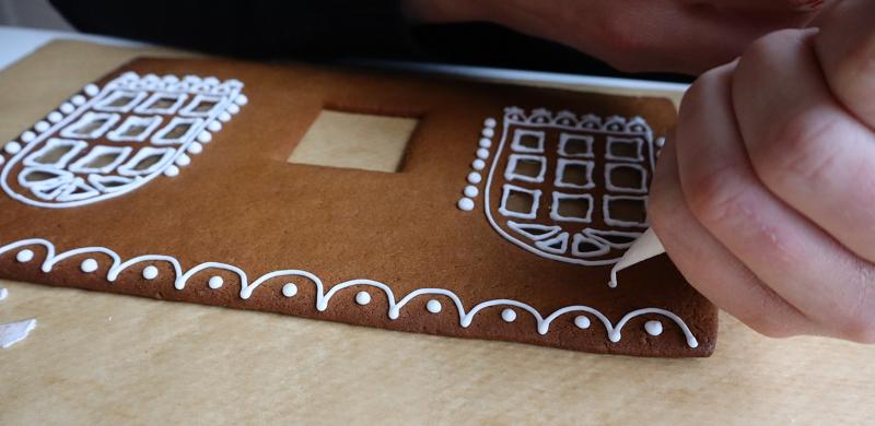En person dekorerar en rektangulär pepparkaksbit med vit glasyr och skapar mönster och konturer på ytan.
