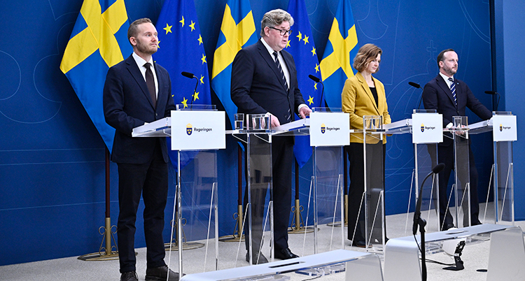Fyra personer står vid varsitt bord. De har varsin mikrofon. Bakom dem finns Sveriges flagga och EUs flagga.