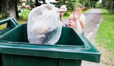 Ett barn kastar en soppåse i en grön soptunna.