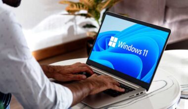 Windows 11 auf einem Laptop auf einem Kaffeetisch mit einem Mann mit Händen auf der Tastatur