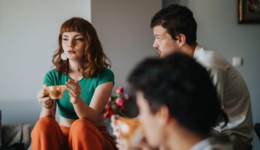 Tre unga personer sitter i hemmiljö och pratar. Ung kvinna med långt hår och tekopp säger något.