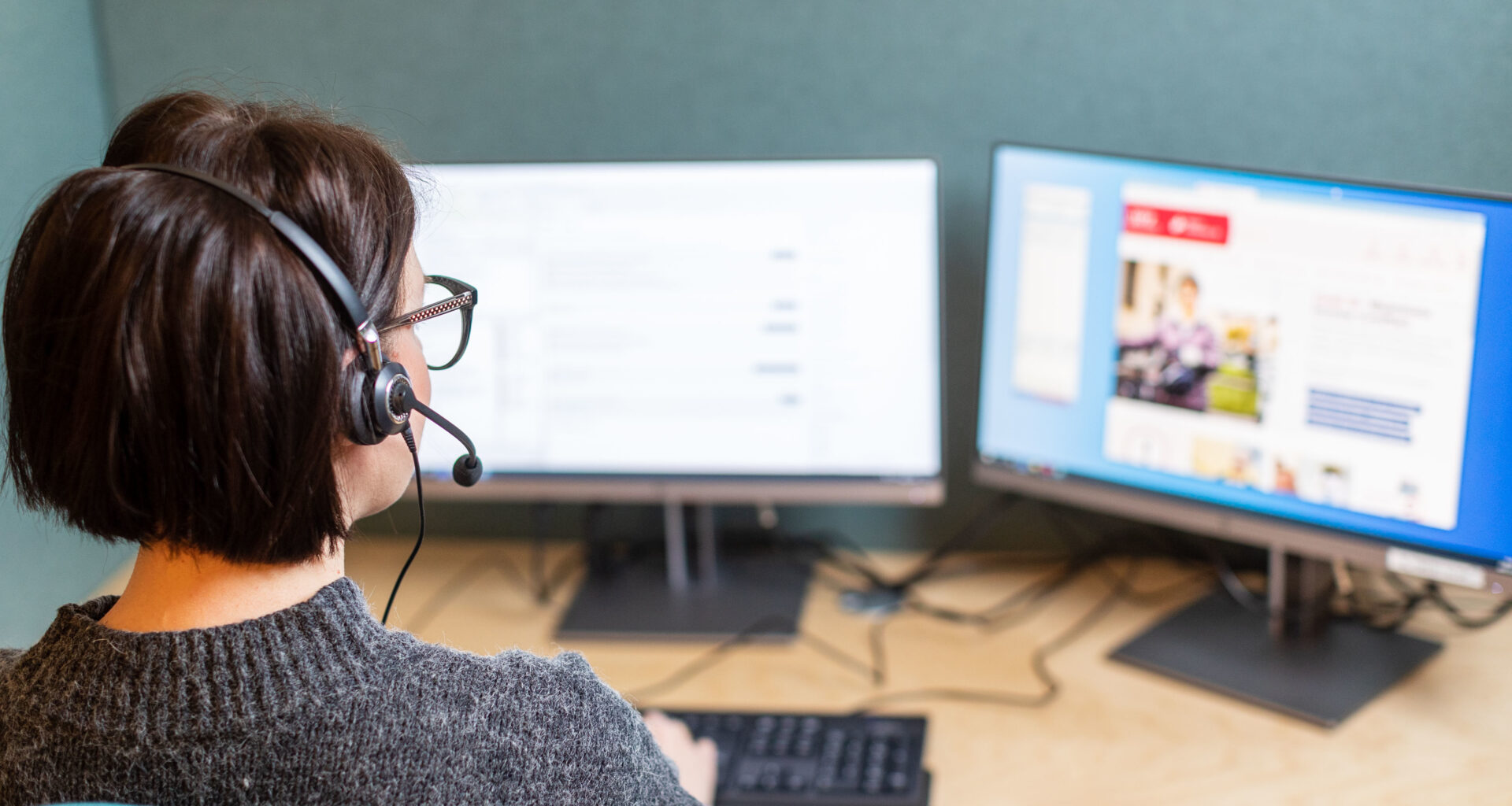 Kvinna med headset sitter framför två datorskärmar.