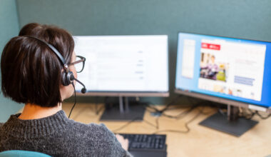 Kvinna med headset sitter framför två datorskärmar.