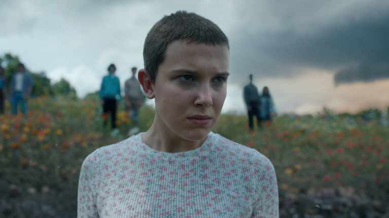 Ung kvinna i ort hår på äng med människor i bakgrunden.