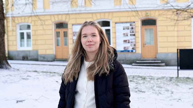 Kvinna står utomhus med snö i bakgrunden. 