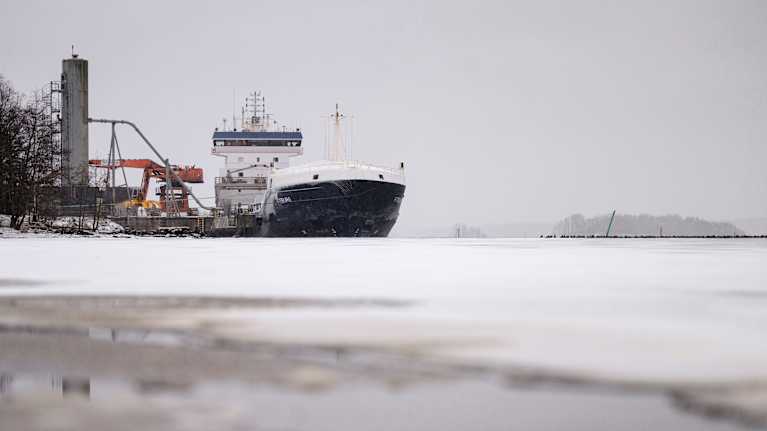 Fraktfartyget Fitburg förtöjd i en hamn. Havet i förgrunden är fruset.