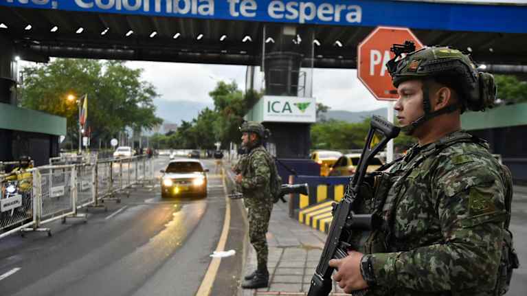Tungt beväpnde soldaer står på en gata nedanför en bro.