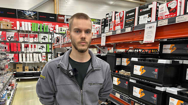 En person står i en butik, omgiven av hyllor fyllda med batterier och andra fordonsrelaterade produkter.