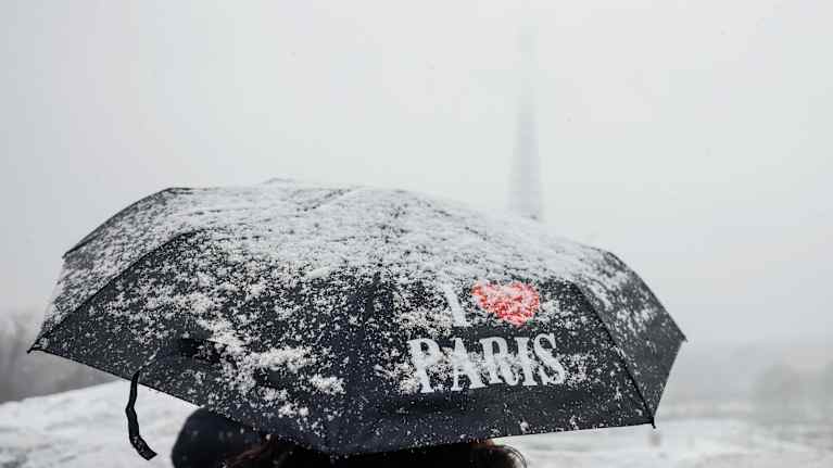 En person går med ett paraply som det står "I Love Paris" på i snöoväder. 