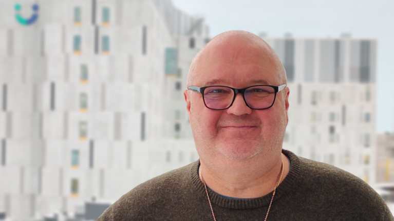 En person står på en balkong med sjukhuset bakgrunden. 