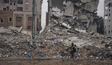 En man på cykel framför trasiga hus.