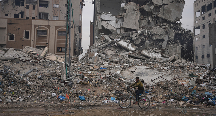 En man på cykel framför trasiga hus.