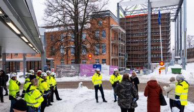Vy över personer samlade utanför en hög byggnad, många med byggarbetskläder på.