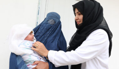 En barnmorska. till höger. undersöker en bebis som hålls av en kvinna i burka.